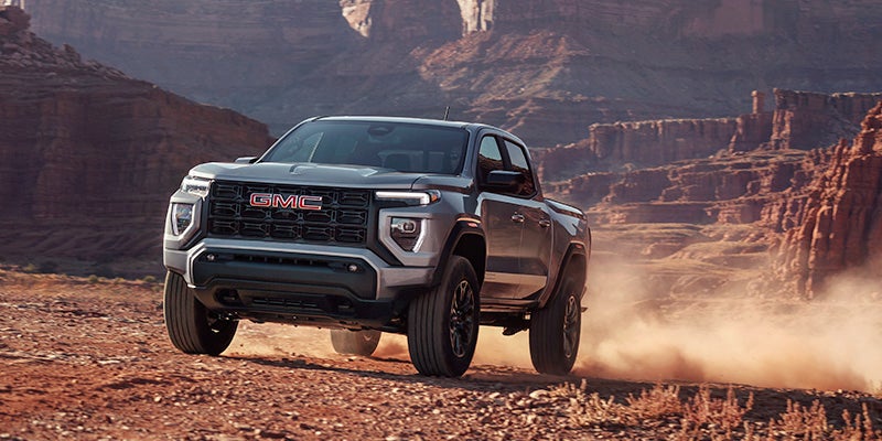 A Silver, GMC Canyon driving , and kicking up dirt.